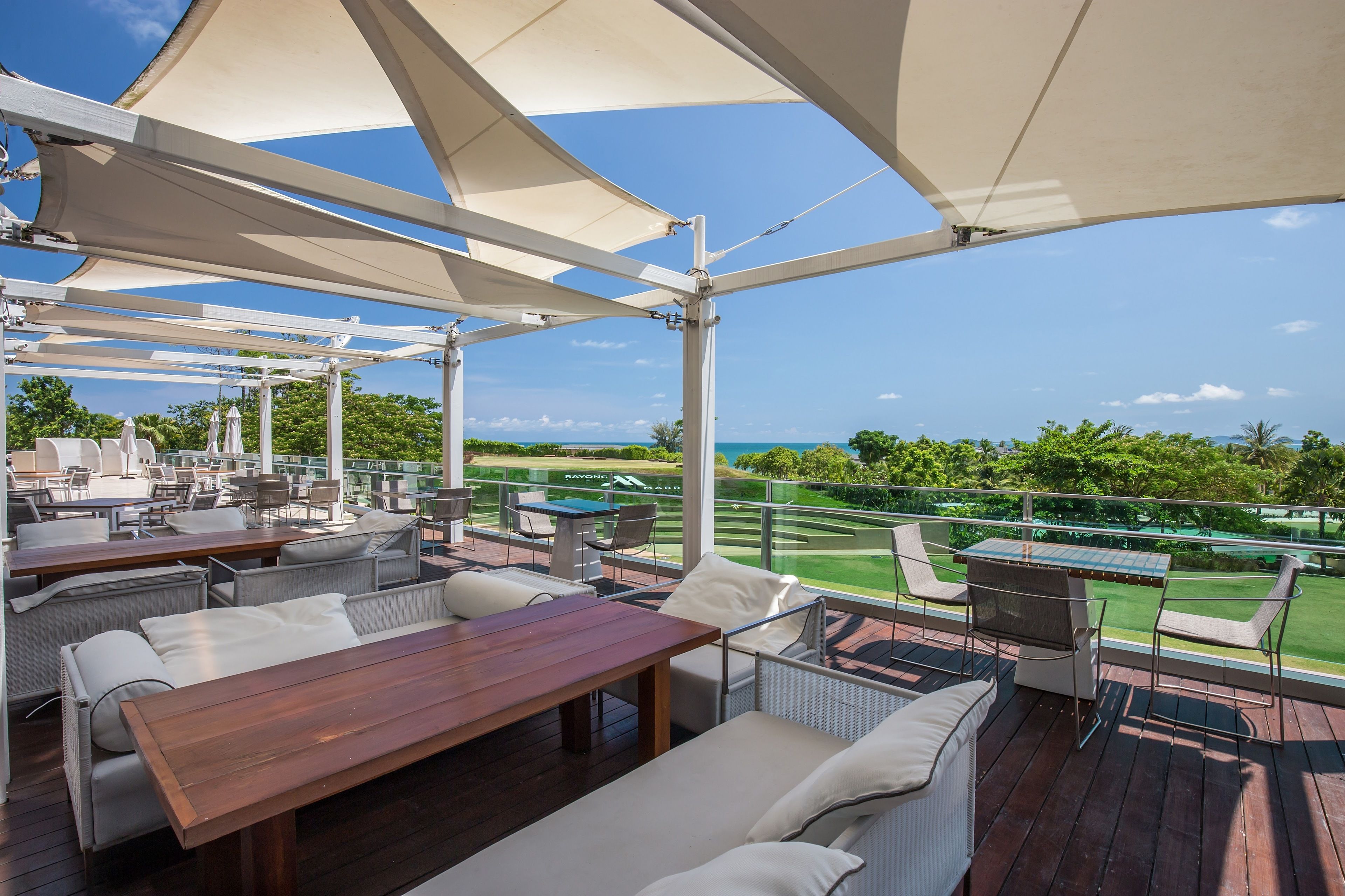 Een terras buiten met tafels en stoelen, een houten terras en uitzicht op een golfbaan.