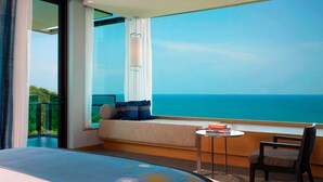 A hotel room with a large bed, a small table with books, a chair, a sofa with a view of the ocean, and a balcony with curtains. - Rayong Marriott Resort & Spa (Klaeng)