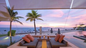 A sunset view from a balcony with a pool, two cushioned seating areas, and a table with a candle. - Rayong Marriott Resort & Spa (Klaeng)