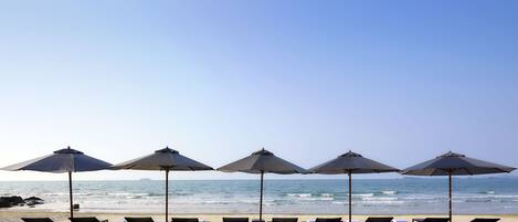 A beach with sun loungers and umbrellas, a clear sky, and the ocean in the background.