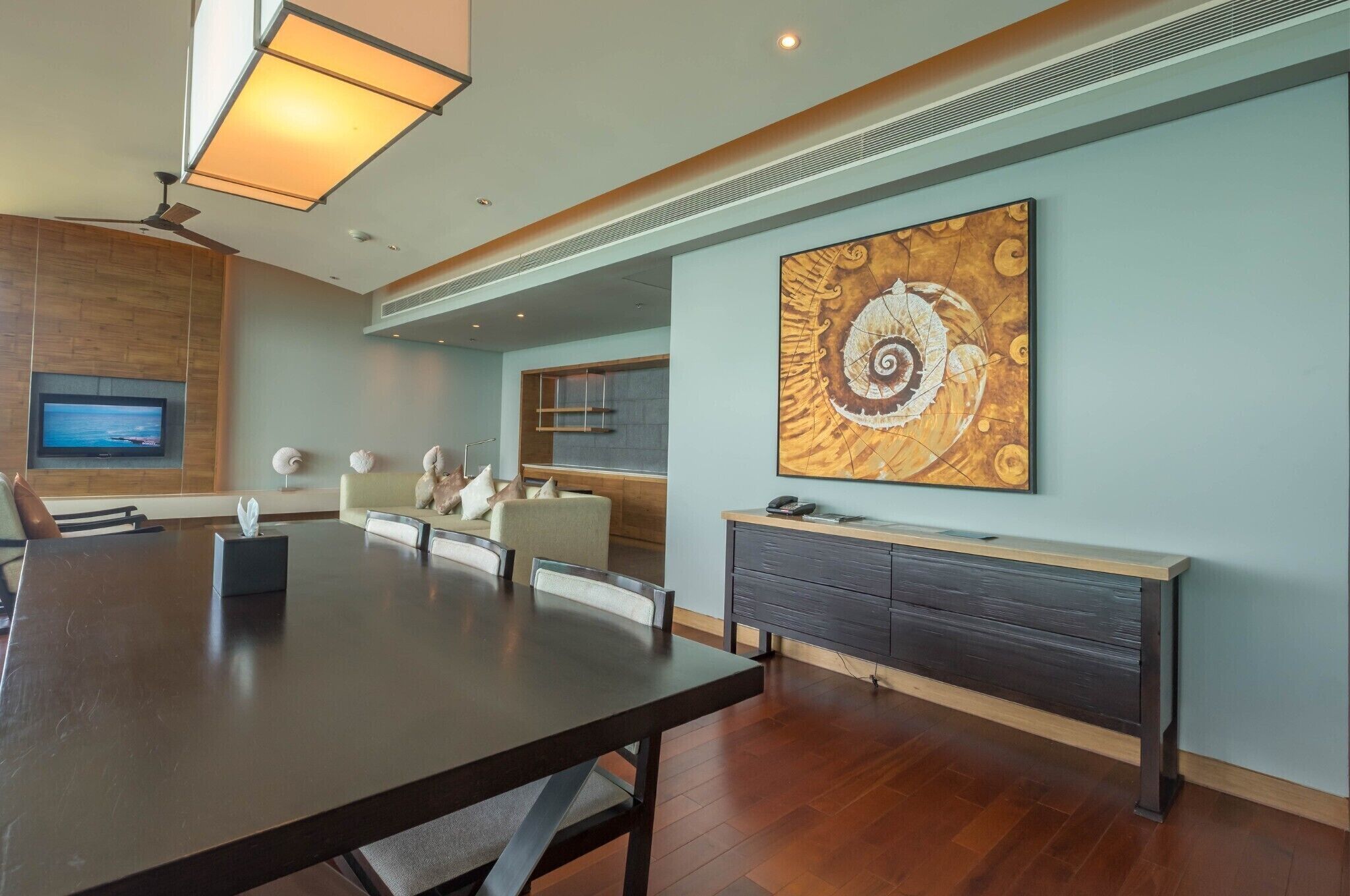 Une salle de réunion moderne, dotée d’une grande table, de sièges confortables, d’un téléviseur à écran plat et d’un tableau décoratif au mur.