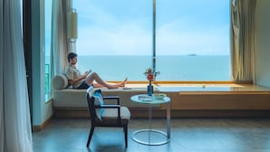 A room with a large window overlooking the sea, a sofa, a chair, and a small table with a vase. - Rayong Marriott Resort & Spa (Klaeng)