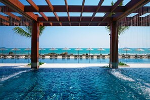 A pool area with clear blue water, lounge chairs, umbrellas, and a view of the ocean.