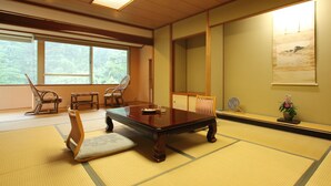 Een traditionele kamer met tatami matten, een lage tafel, stoelen en een groot raam met uitzicht op groen.