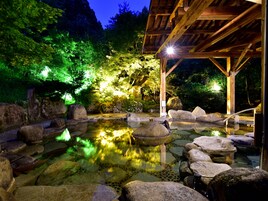 A tranquil outdoor hot spring area with wooden structures and large rocks.
