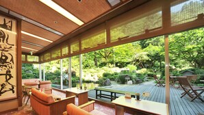 Een traditionele Japanse kamer met tatami vloerbedekking, een lage houten tafel en uitzicht op een weelderige tuin.