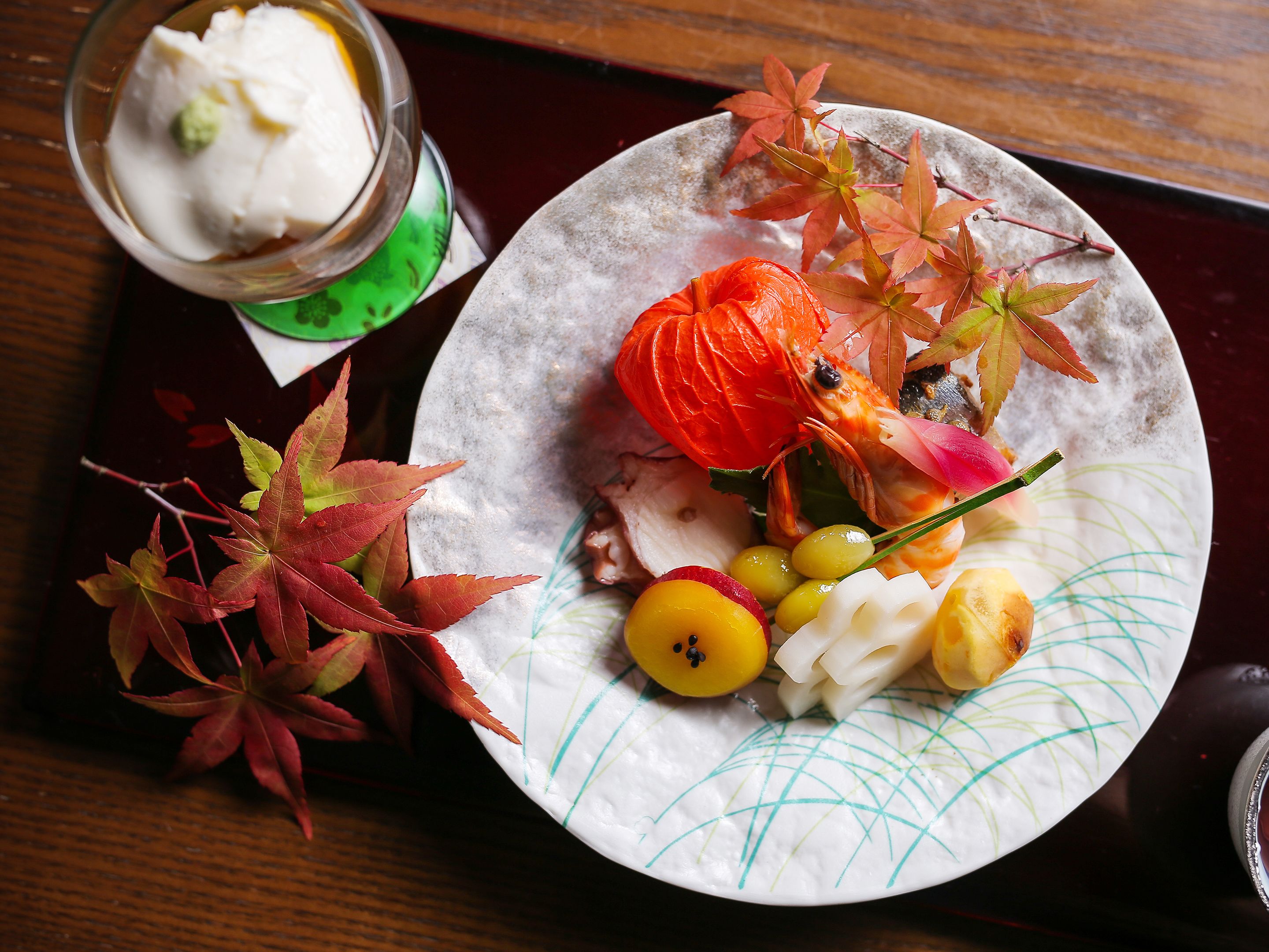 A plate with a variety of food items including a whole shrimp, a red lantern, and some leaves.