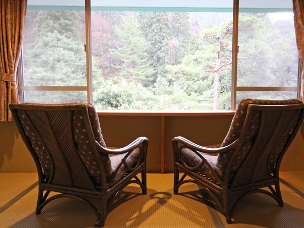 Two wicker chairs facing a window with a view of a forest.