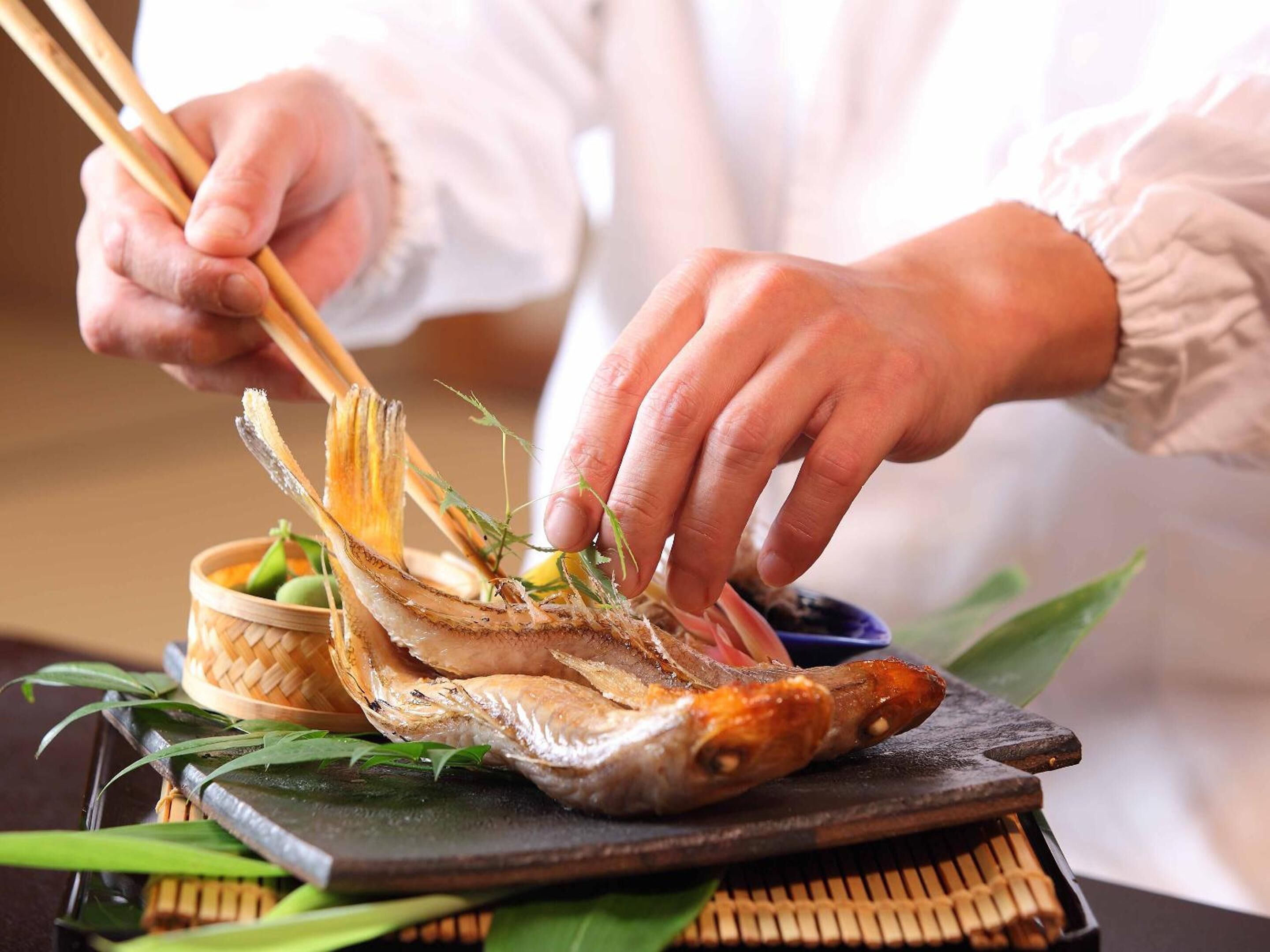 Una persona usando palillos para tomar un pescado de una cesta tejida.
