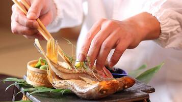 Una persona usando palillos para tomar un pescado de una cesta tejida.