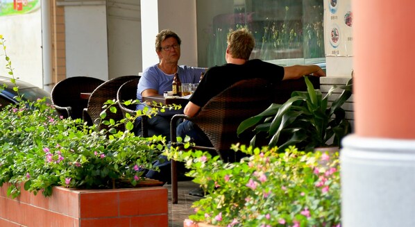 Two people seated at a table in an outdoor cafe area with potted plants and a brick wall. - Guangzhou Masia Hotel (Guangzhou)