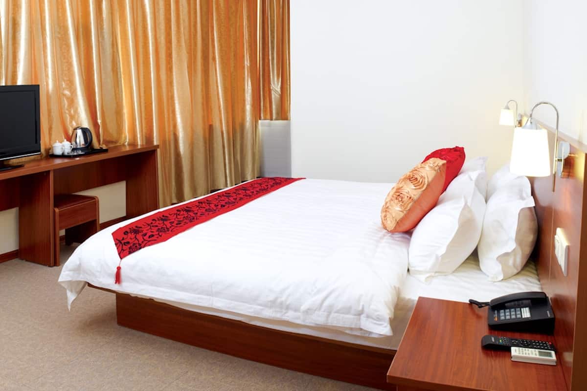 A hotel room with a bed, a desk with a TV, a telephone, and a lamp.