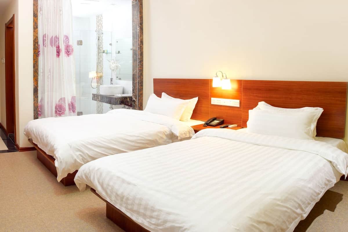 A hotel room with two beds, a wooden headboard, a bedside telephone, and a bathroom visible through a glass door.