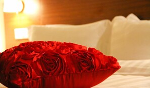A bed with white linens and a red rose pillow.