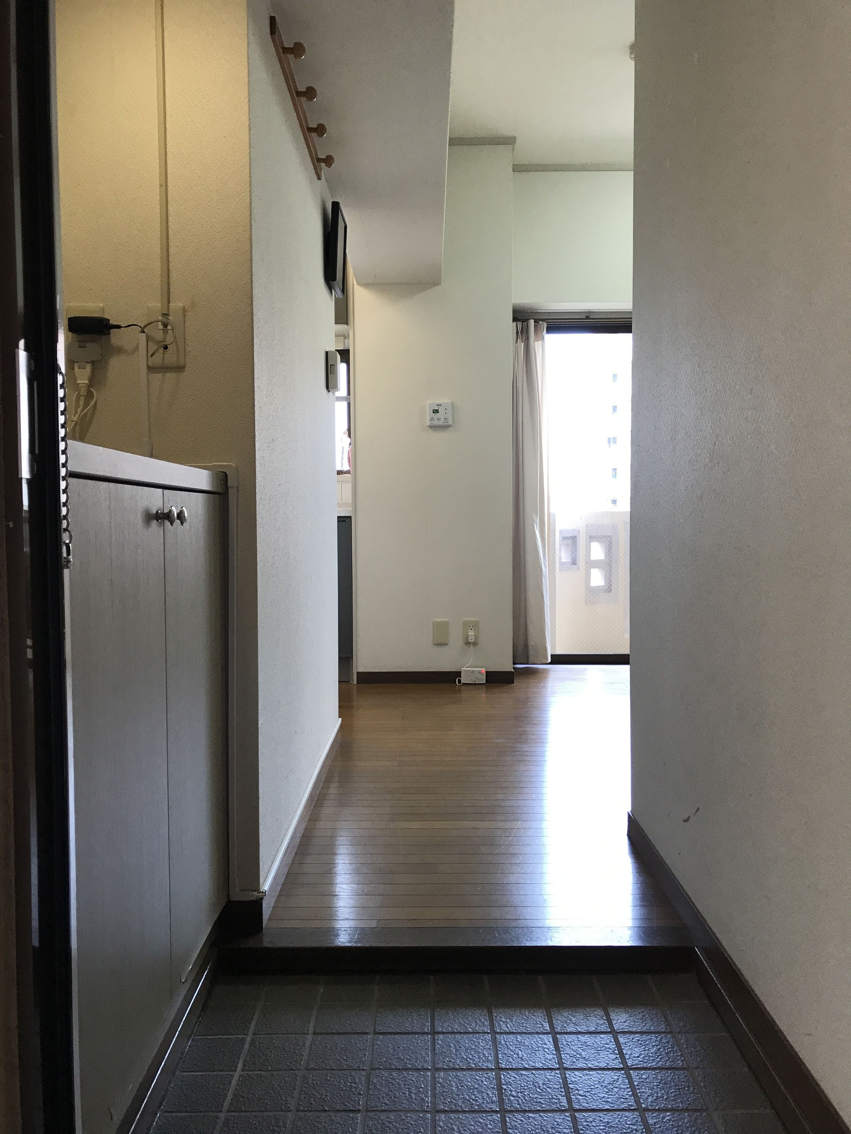 A hallway with a wooden floor, a kitchen area with cabinets, and a view of a building outside.
