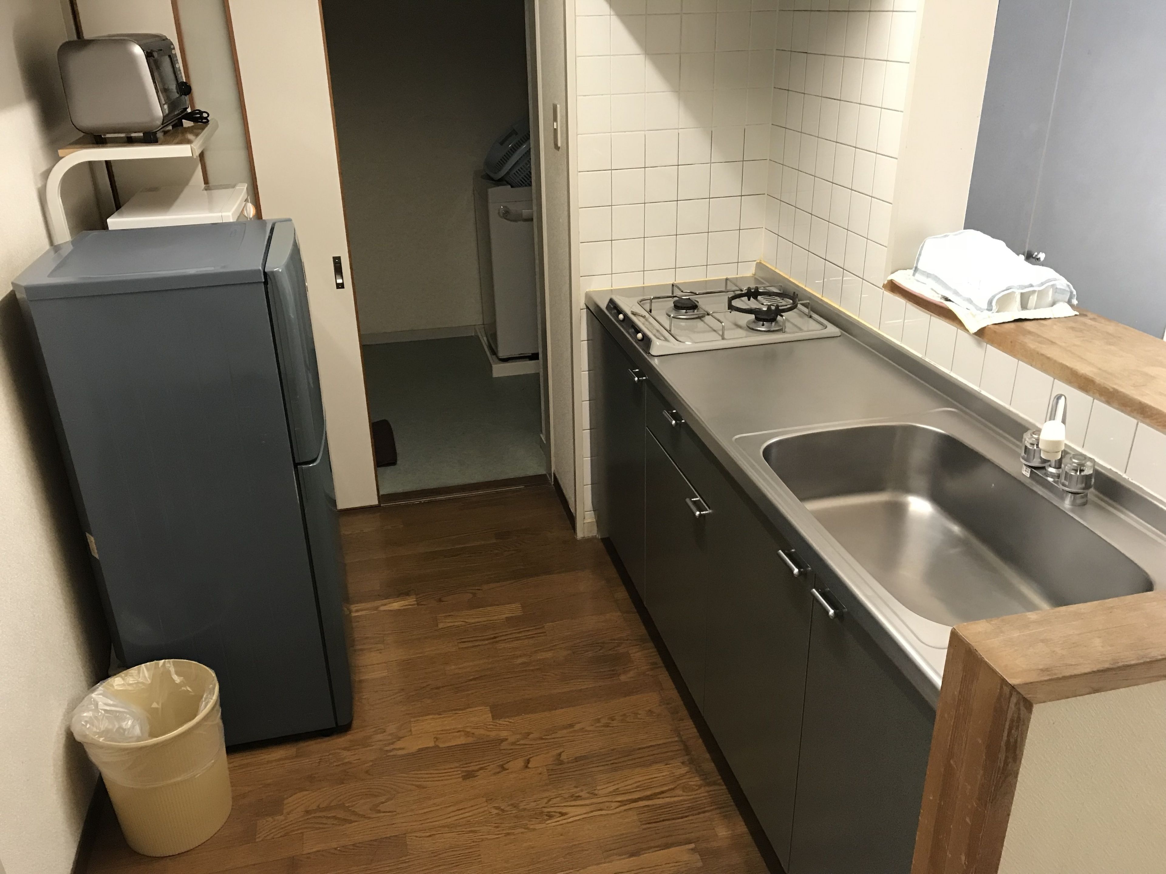 A compact kitchen with a refrigerator, stove, sink, and wooden flooring.