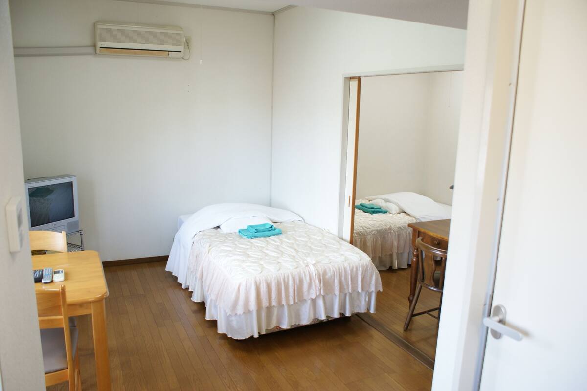A small, clean room with a single bed, a desk, a chair, and a television.