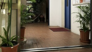 A hallway with potted plants, a blue door, and a bulletin board with notices. - Weekly Harborview Mansion - Main Building (Naha)