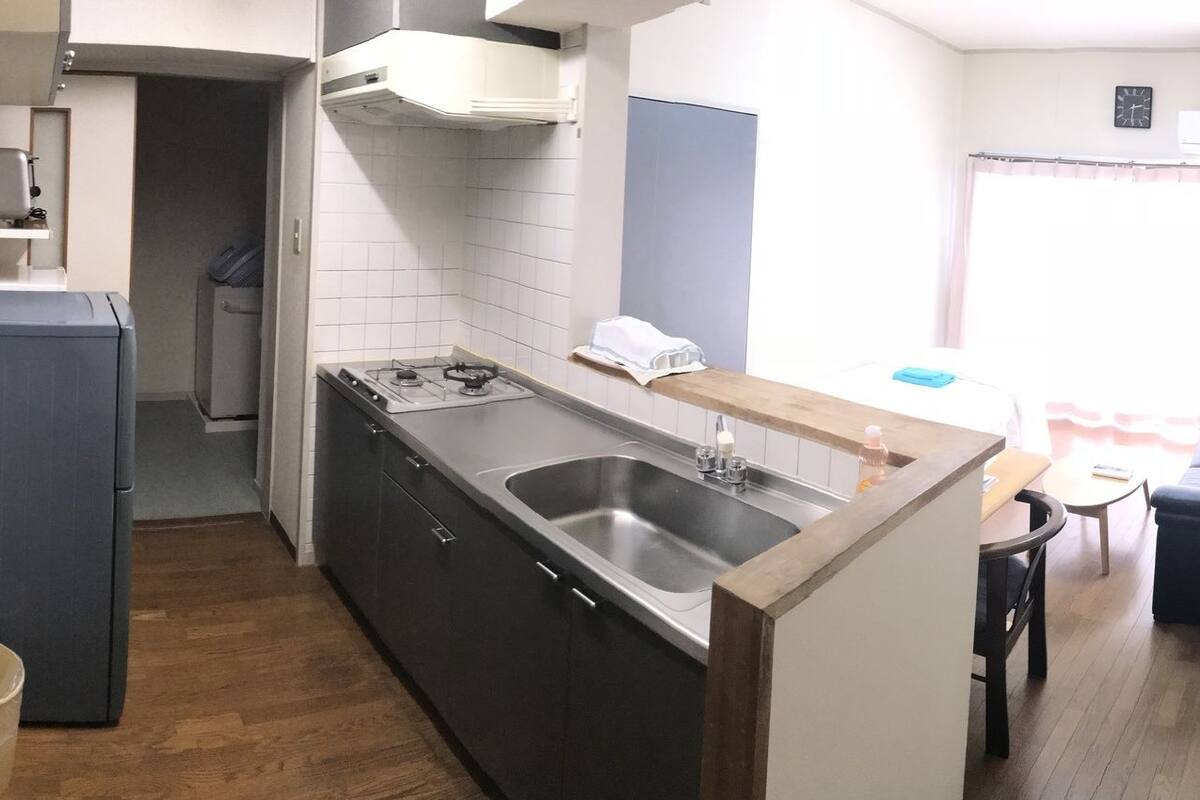 A compact room with a bed, a small kitchenette, a sink, and a seating area with a TV.