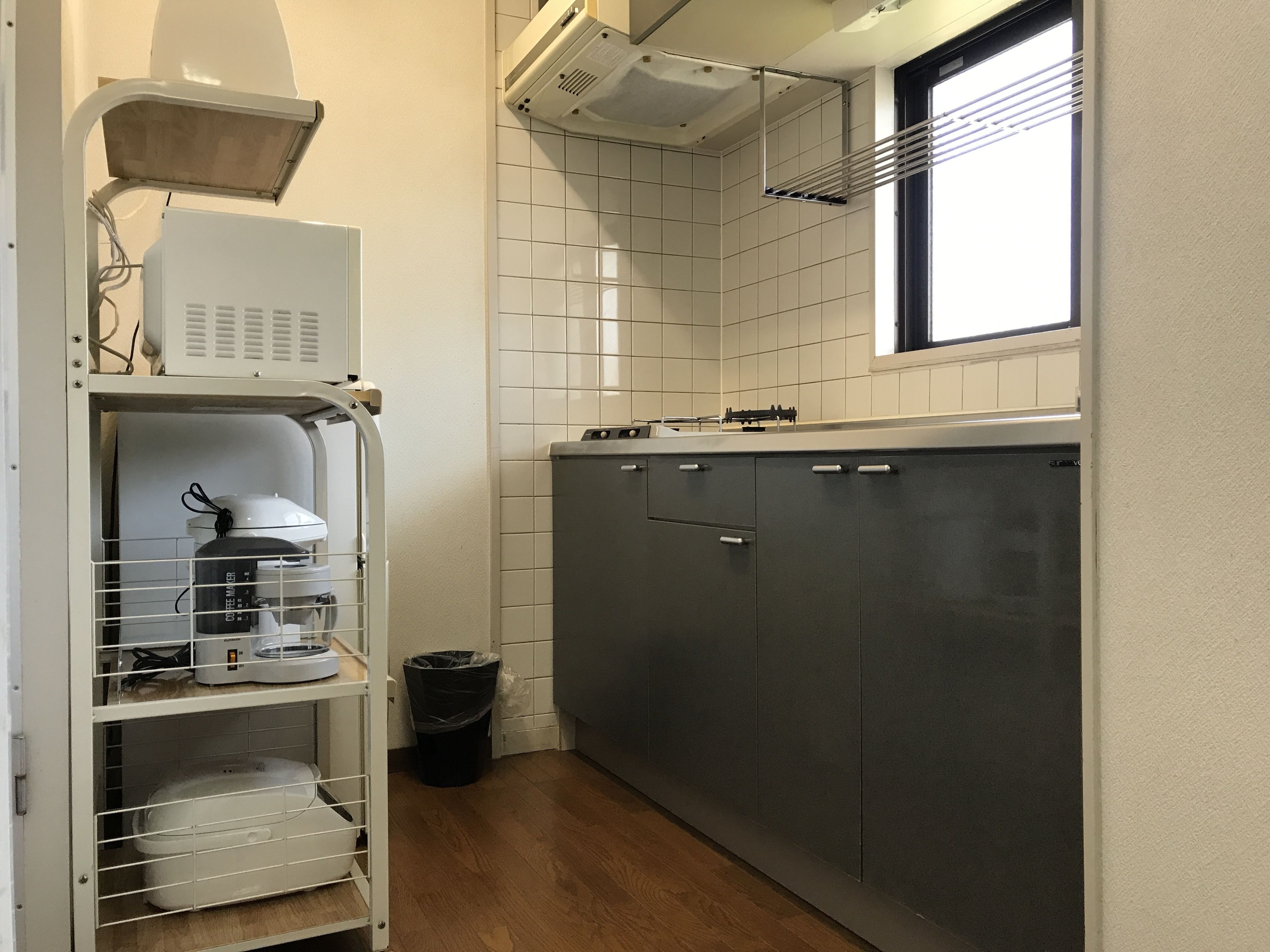 A compact kitchen with a built-in oven, a coffee maker, and a small trash bin.