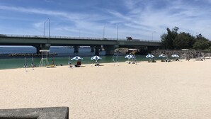 A beach with a bridge in the background, beach umbrellas, and a lifeguard tower. - Weekly Harborview Mansion - Main Building (Naha)