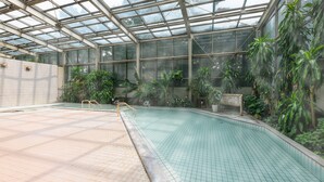 An indoor swimming pool with a glass ceiling, surrounded by potted plants and a bench. - Hotel Kirishima Castle (Kirishima)