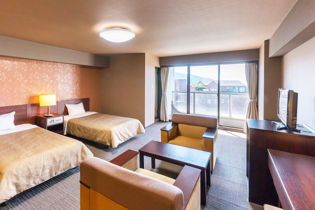 A hotel room with two beds, a desk, a chair, a TV, and a large window.