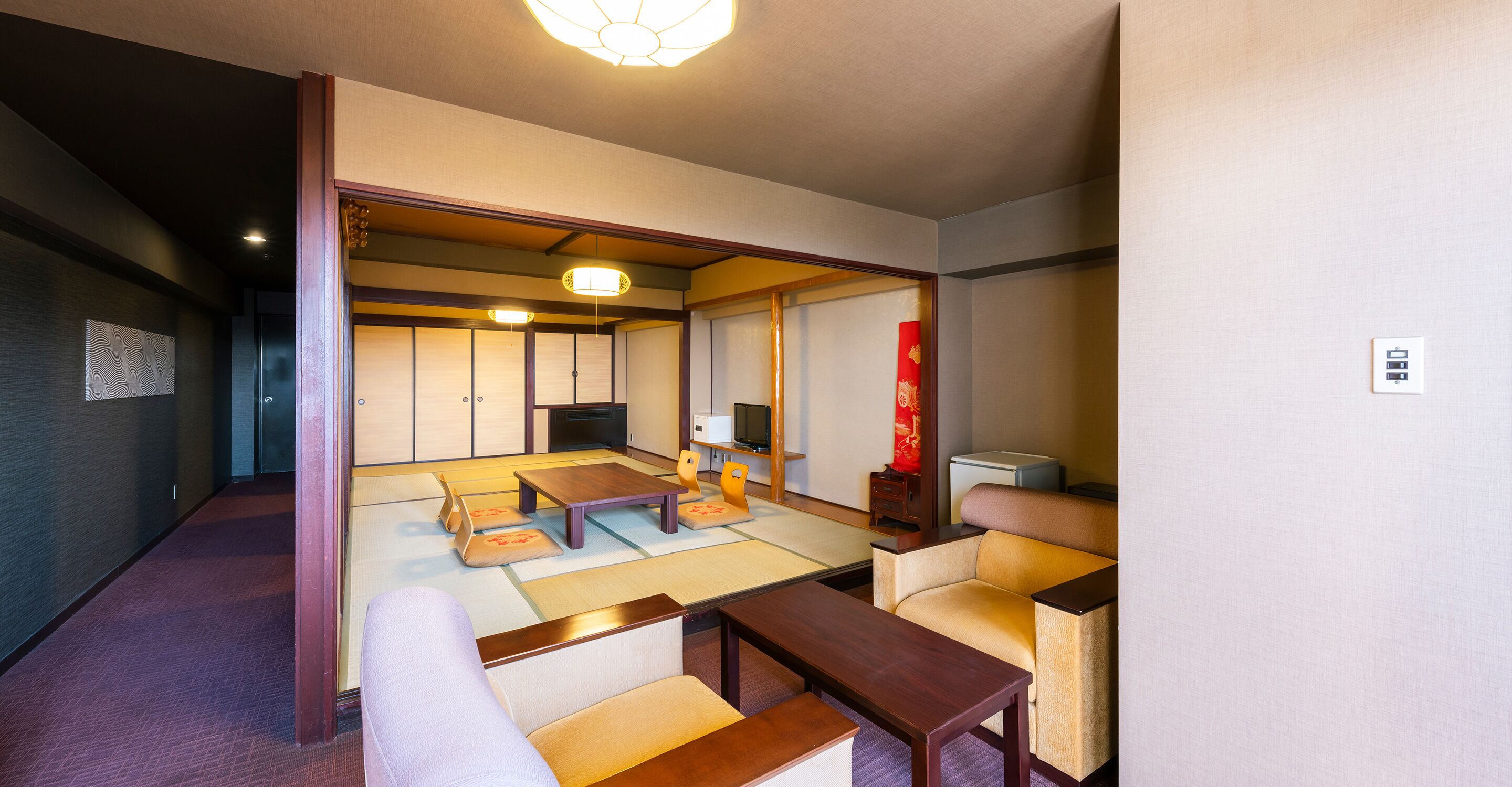 Una habitación tradicional japonesa con suelo de tatami, una mesa baja de madera, un sofá y un televisor.