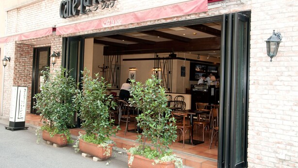 Café con mesas al aire libre, paredes de ladrillo y plantas en macetas.