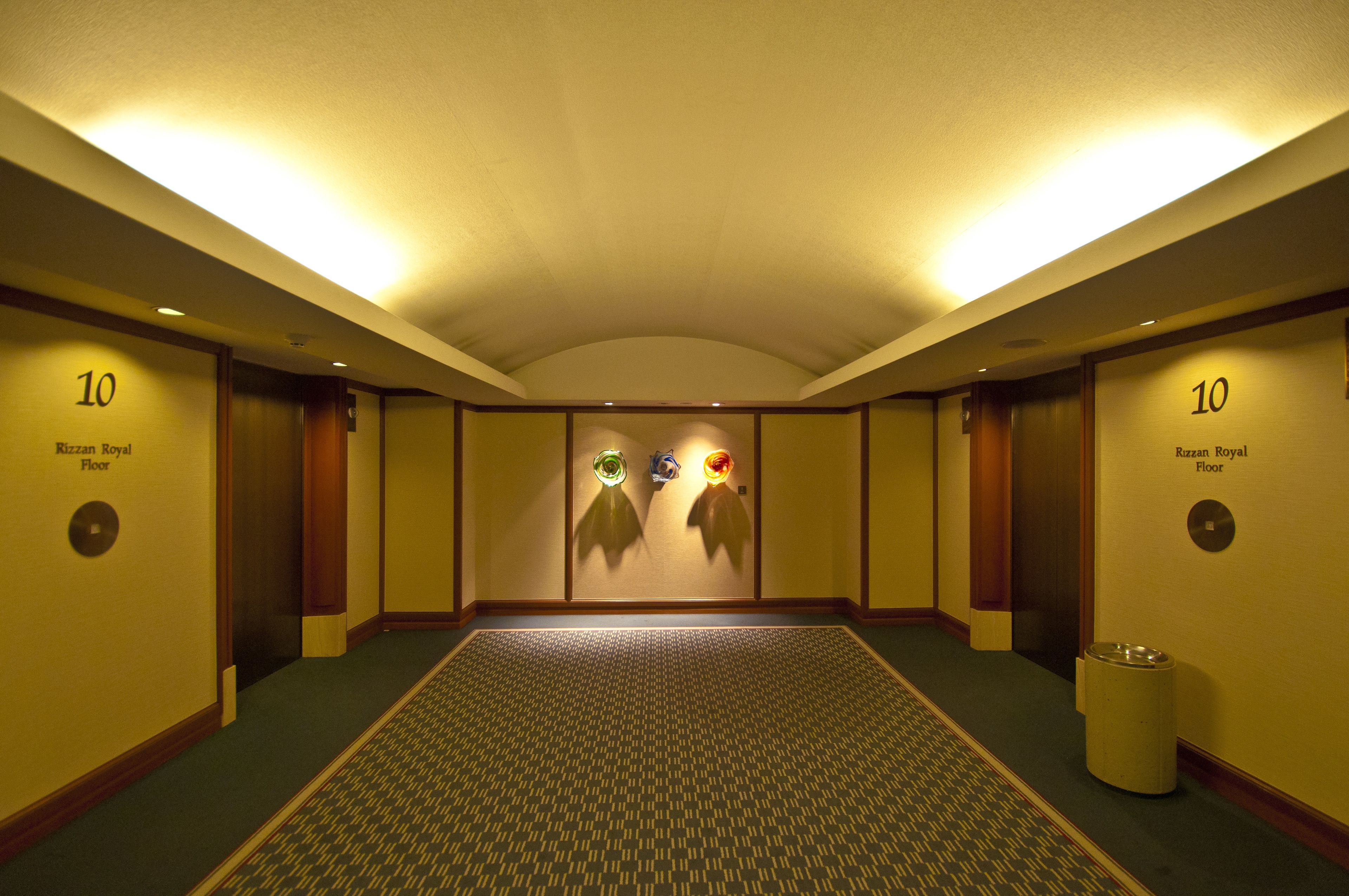 A hotel corridor with a patterned carpet, two doors labeled "10", and a trash can.