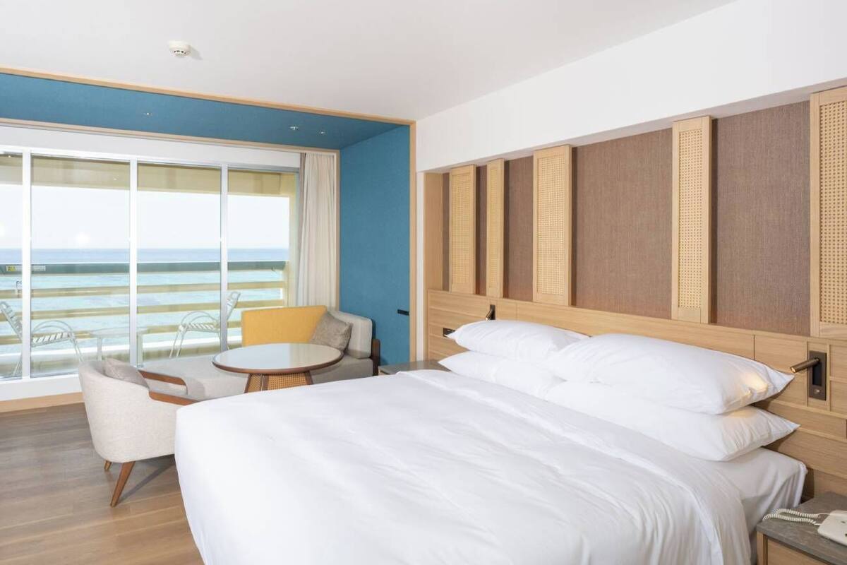 A hotel room with a large bed, a small round table, a sofa, and a view of the ocean.