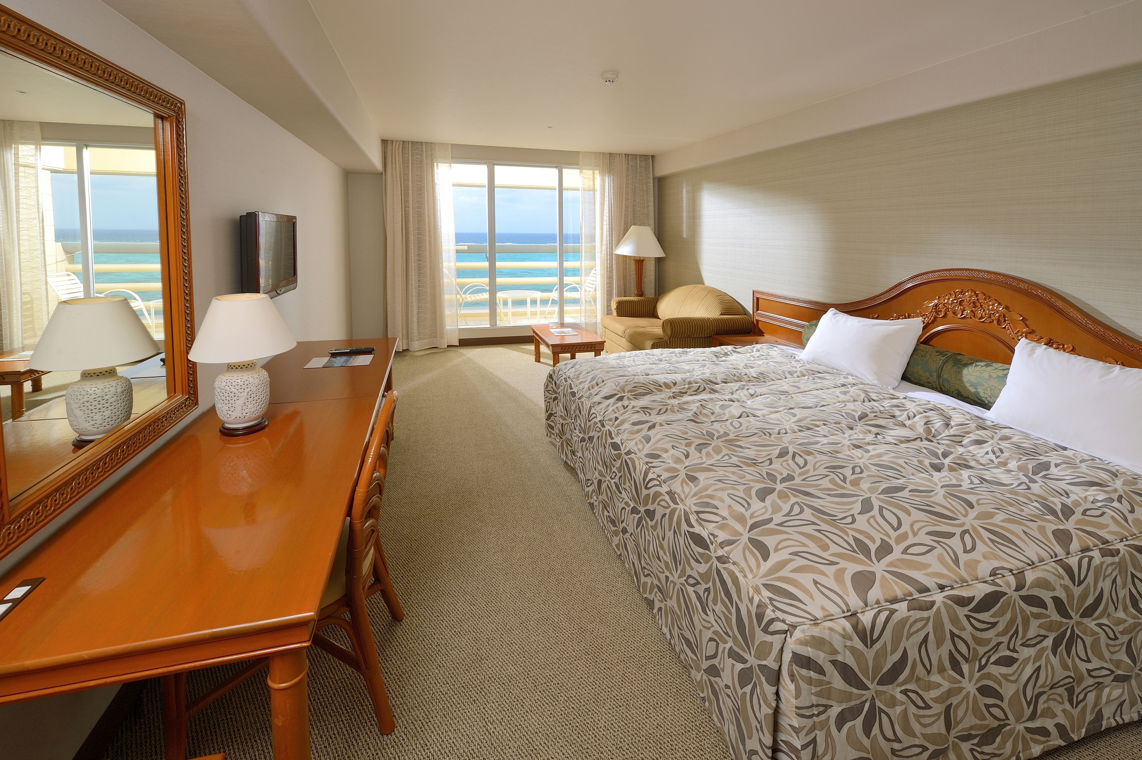 Una habitación de hotel con cama, escritorio con lámpara, televisión y vista a la playa.