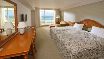 Una habitación de hotel con cama, escritorio con lámpara, televisión y vista a la playa.