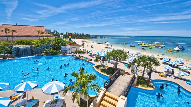 A resort with a large swimming pool, beach area, and palm trees. - Rizzan Sea Park Hotel Tancha Bay (Onna)