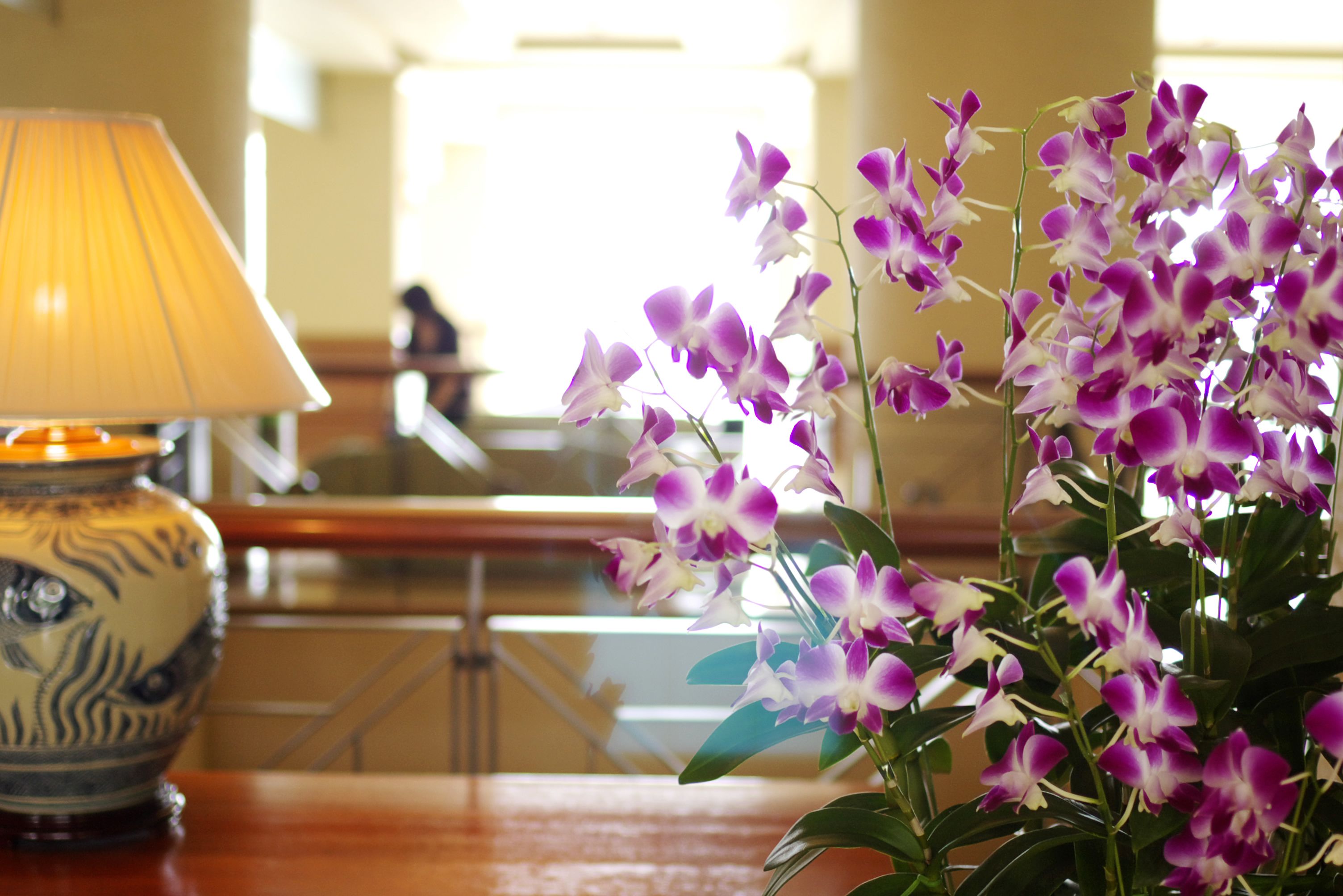 A table with a lamp and a vase of purple orchids.