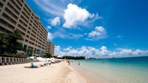 A beach with a hotel on the left, clear blue sky, and calm sea. - Rizzan Sea Park Hotel Tancha Bay (Onna)