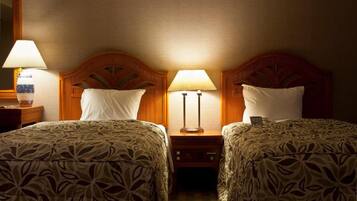 A hotel room with two beds, each with a patterned bedspread and a wooden headboard. There are two bedside lamps and a nightstand with a lamp between the beds.