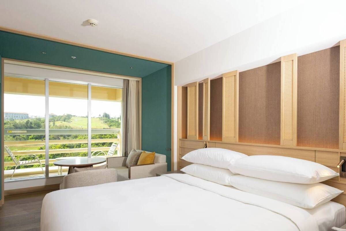 A hotel room with a large bed, a seating area with a view, and a window overlooking a green landscape.