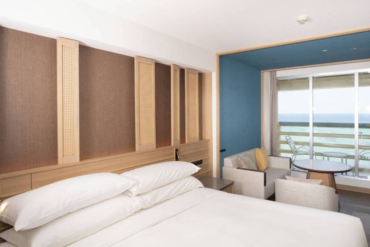 A hotel room with a bed, a seating area with a table, and a view of the ocean.