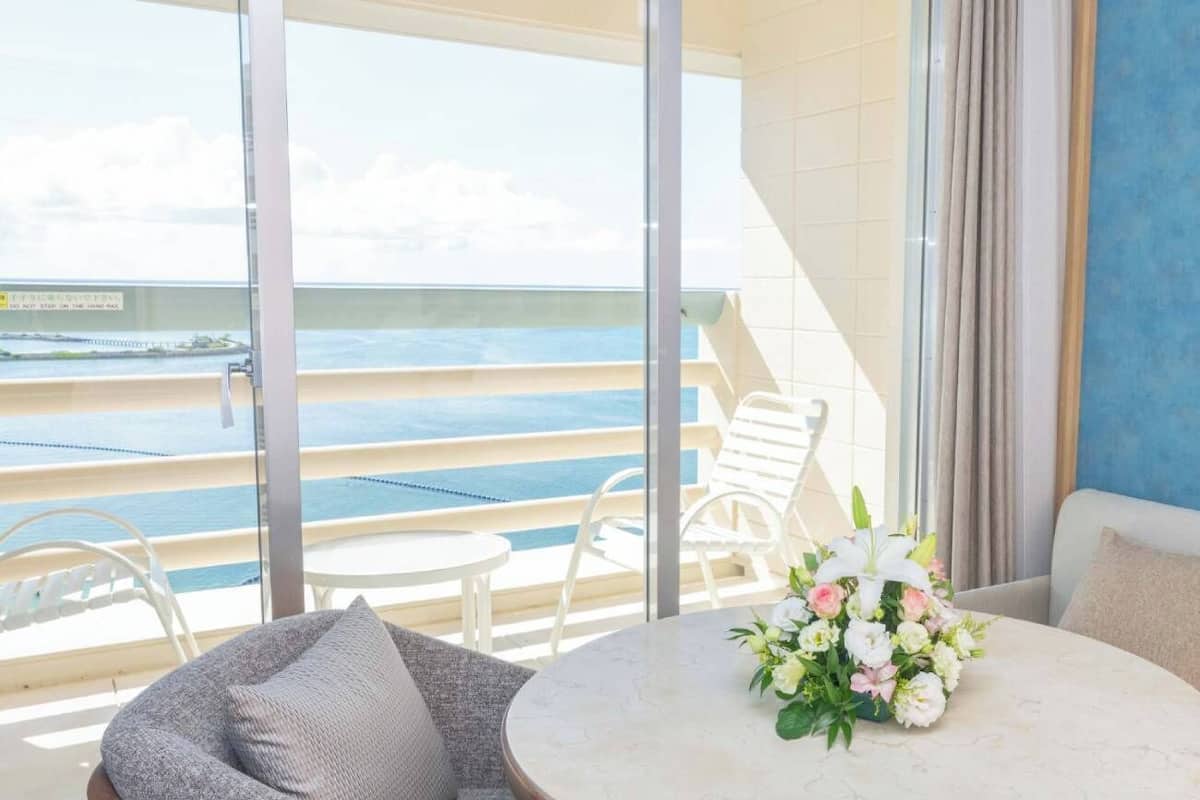 A balcony with a view of the sea, a round table with a floral arrangement, and white lounge chairs.