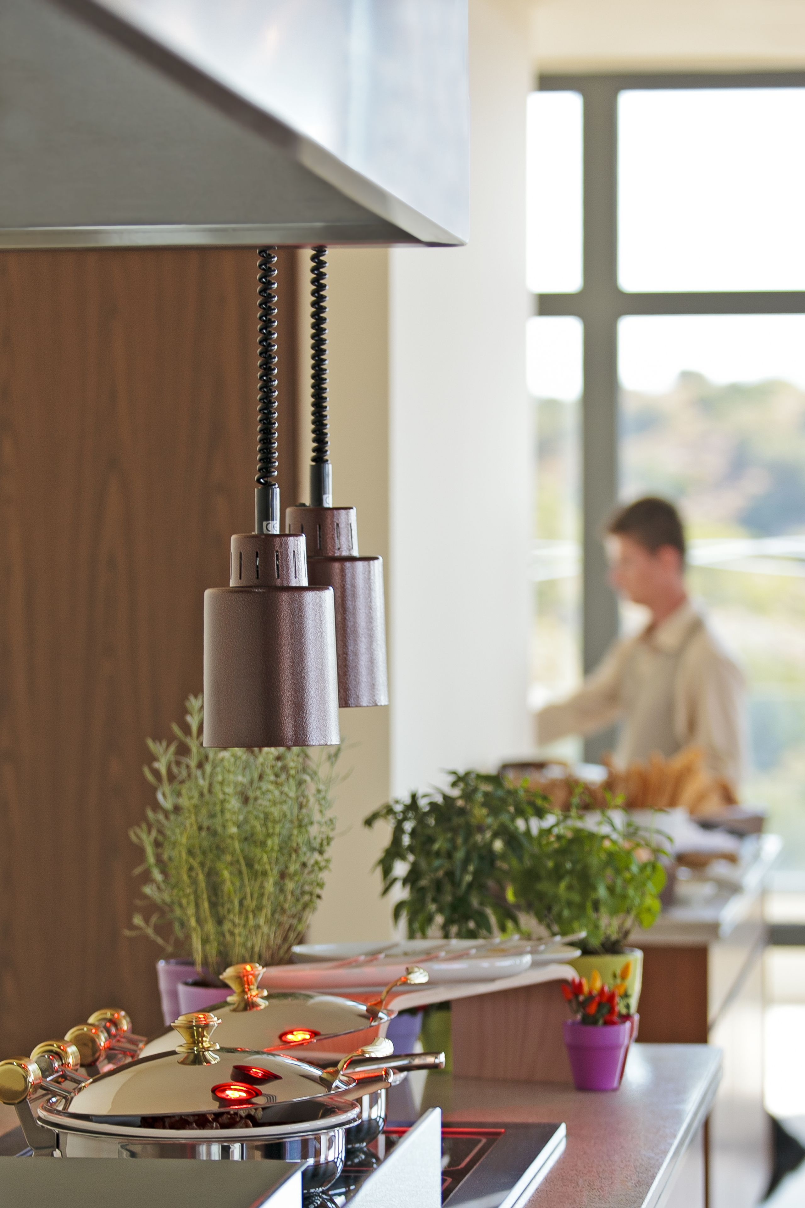 Una cocina moderna con electrodomésticos de acero inoxidable, una lámpara colgante y vistas a una persona trabajando en la encimera.