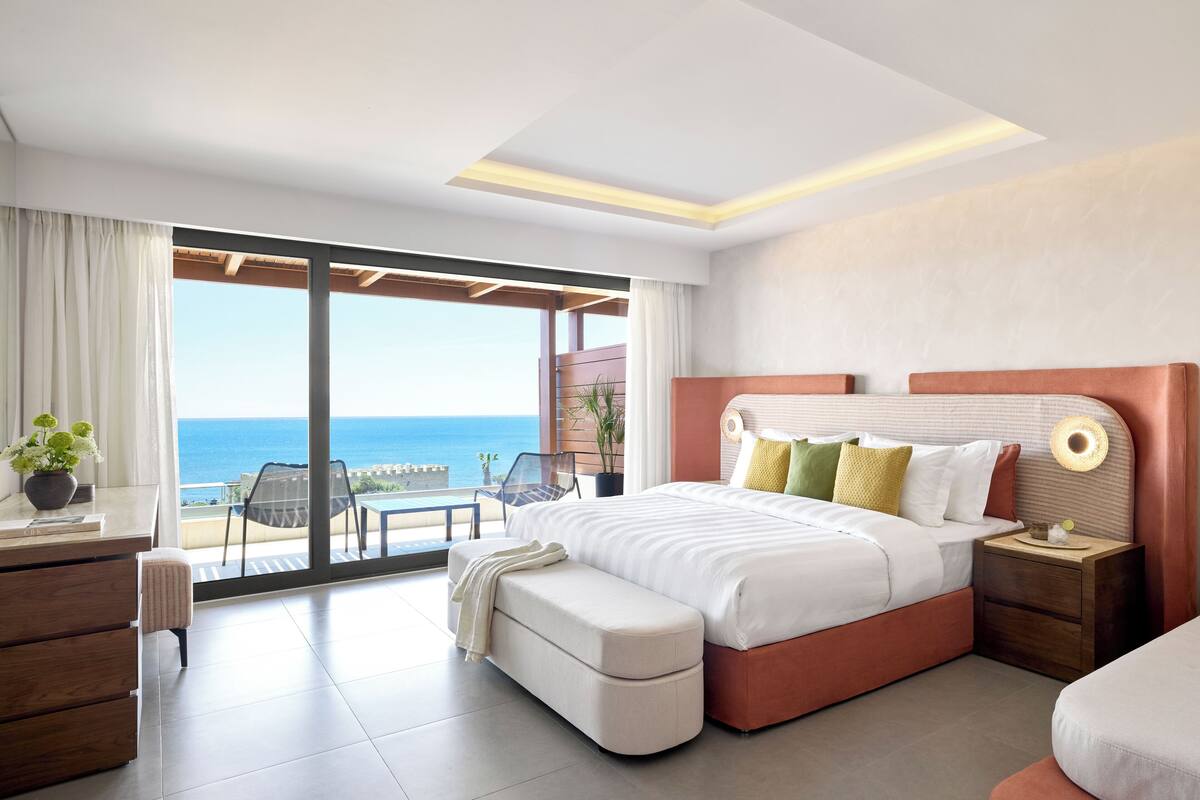 Ein modernes Schlafzimmer mit einem großen Bett, einem Schreibtisch und Blick auf das Meer.