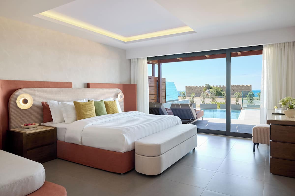 Ein modernes Hotelzimmer mit einem großen Bett, einem Schreibtisch und Blick auf einen Pool und eine Burg.