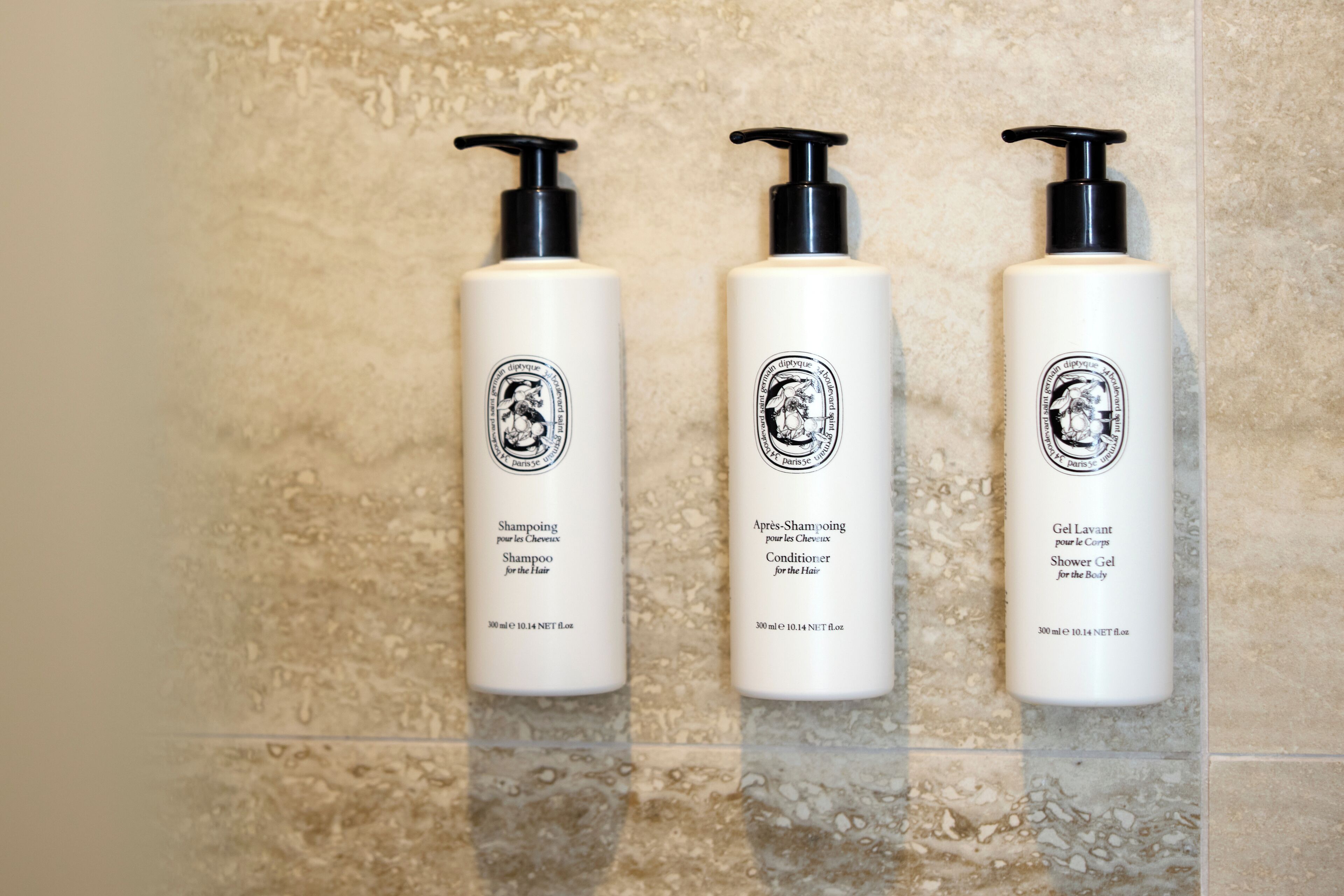 Tres botellas de productos para el cabello sobre un muro de azulejos.