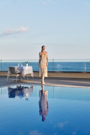Eine Person steht am Pool, in der Nähe befinden sich ein Tisch und Stühle mit Blick auf ein Gewässer.