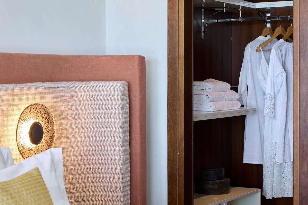 Ein ordentlich eingerichtetes Hotelzimmer mit Bett, Nachttisch und begehbarem Kleiderschrank.