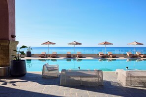 Ein Poolbereich mit Liegestühlen und Sonnenschirmen mit Blick auf das klare, blaue Meer.