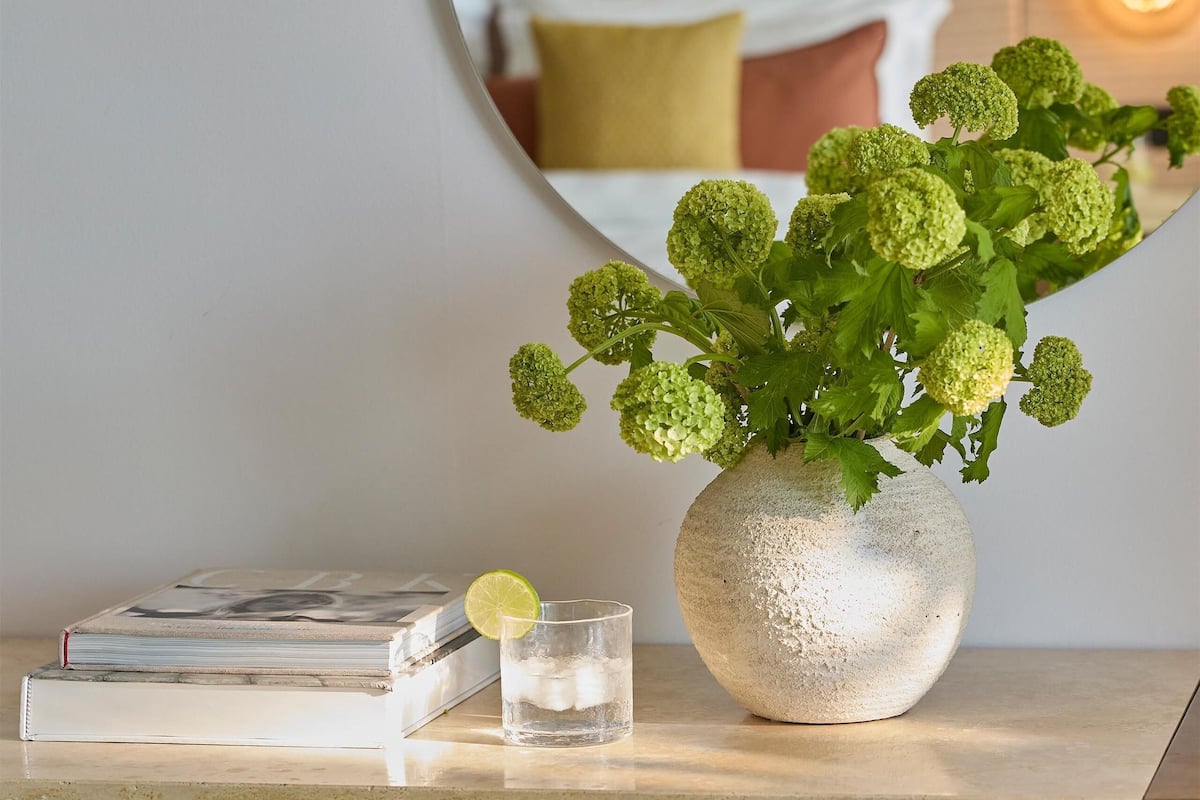 Ein ordentlich arrangierter Schreibtisch mit einer Vase mit Grünpflanzen, einem Glas Wasser und einem Buch.