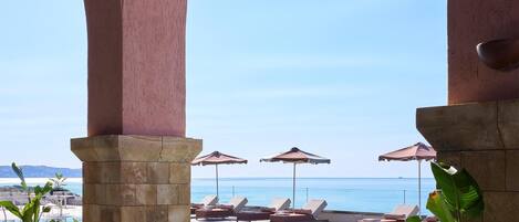 A poolside area with lounge chairs and umbrellas, overlooking a clear blue sea.