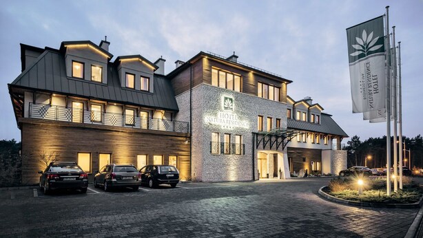 Een hotel met een modern design, met een opvallend bord en meerdere auto's voor de deur.